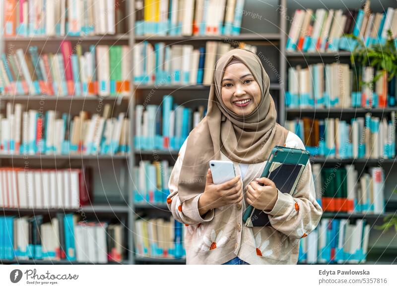 Portrait of asian muslim female student standing in a library real people teenager campus positive exam knowledge confident academic adult lifestyle academy