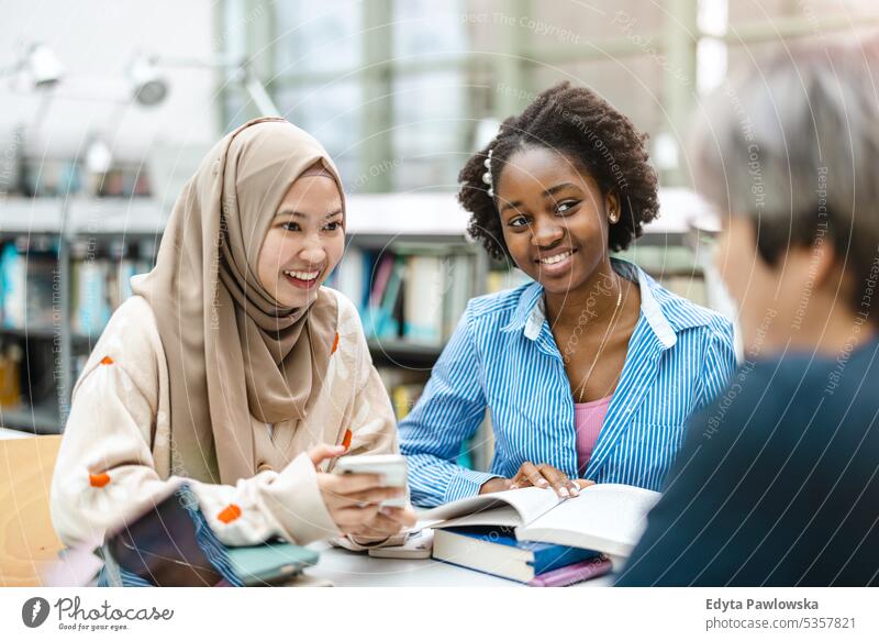 Multiethnic group of students sitting in a library and studying together real people teenager campus positive exam knowledge confident academic adult lifestyle