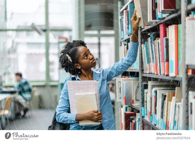 Black female student picking book from bookshelf in library real people teenager campus positive exam knowledge confident academic adult lifestyle academy