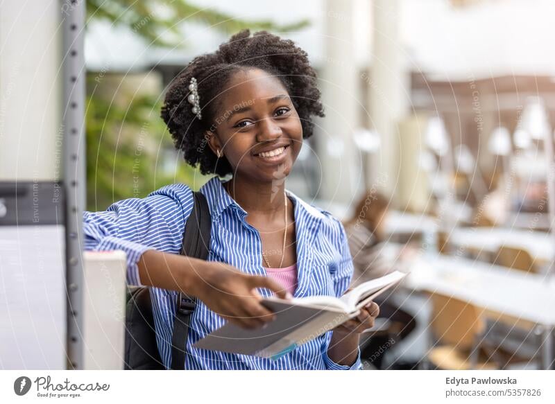 Black female student reading a book in a library real people teenager campus positive exam knowledge confident academic adult lifestyle academy adolescent