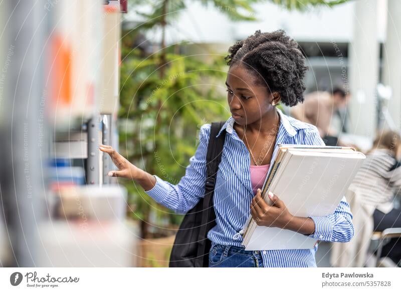 Black female student picking book from bookshelf in library real people teenager campus positive exam knowledge confident academic adult lifestyle academy