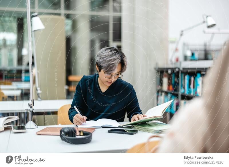 Asian student writing in notebook at table in library real people teenager campus positive exam knowledge confident academic adult lifestyle academy adolescent