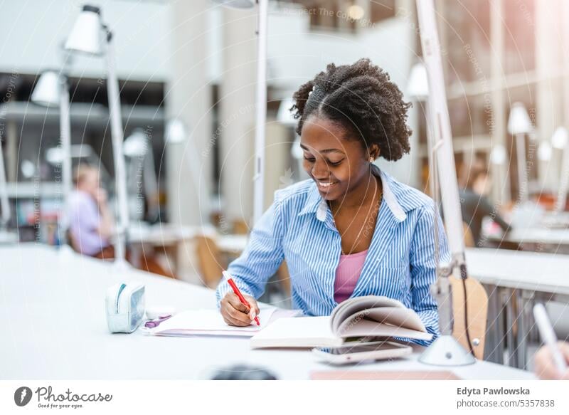 Young black woman writing in notebook in a library real people teenager campus positive exam knowledge confident academic adult lifestyle academy adolescent