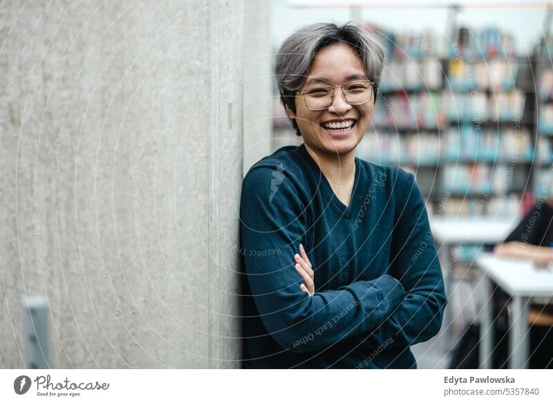 Portrait of smiling asian student standing with arms crossed in college library real people teenager campus positive exam knowledge confident academic adult