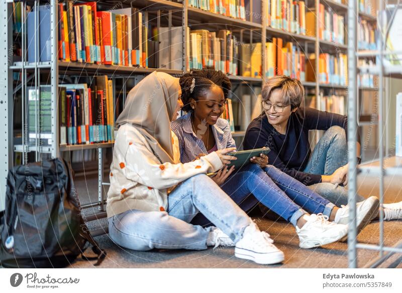 Multiethnic group of students sitting in a library and studying together real people teenager campus positive exam knowledge confident academic adult lifestyle