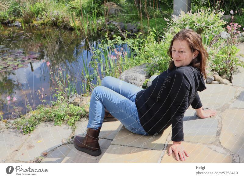 Mainfux-UT | long haired woman sitting casually on stone steps by garden pond Human being Woman feminine Feminine Garden Terrace stagger Pond Garden pond Plant