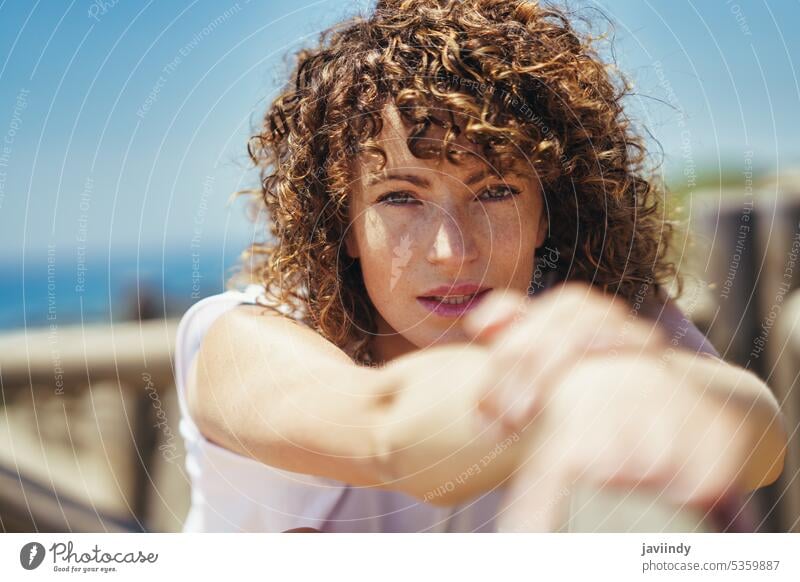 Young woman stretching arms on bridge pensive freckle curly hair portrait wavy hair calm casual fence brown hair posture alone lean brunette lonely human face