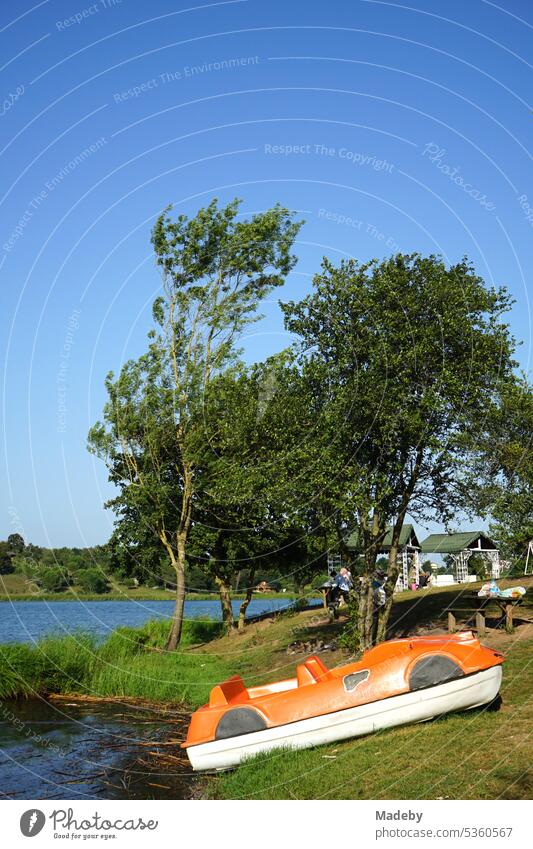 Old plastic paddle boat in orange on shore and jetty in summer against blue sky in sunshine at Poyrazlar Gölü near Adapazari in Sakarya province, Turkey Pedalo