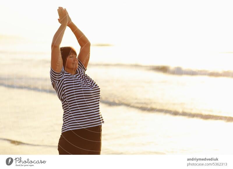 Yoga and meditation of mature woman practicing breath exercises on the sea beach on sunrise in the morning. Body mind and spirit, mindfulness concept. Enlightenment and healthy lifestyle.