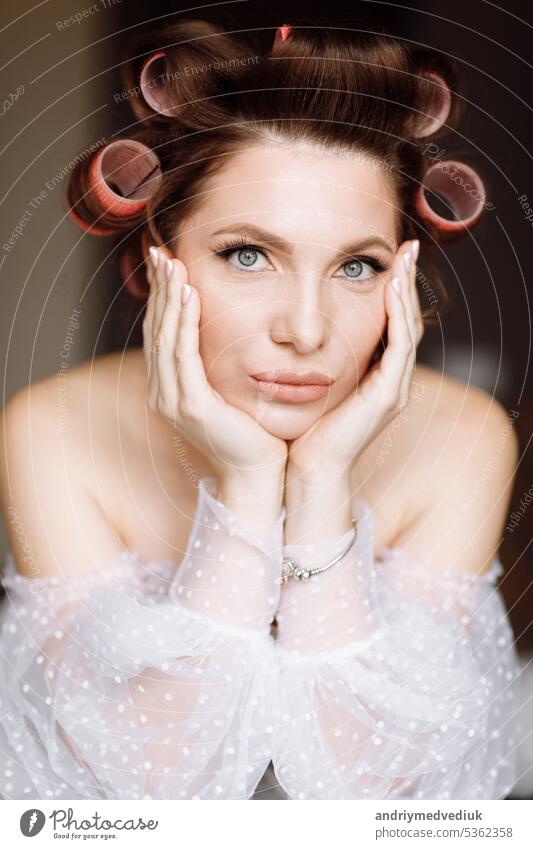 A beautiful young showy brunette woman with bright pin-up make-up in long white lace dress and pink curlers. beauty concept. international women's day march