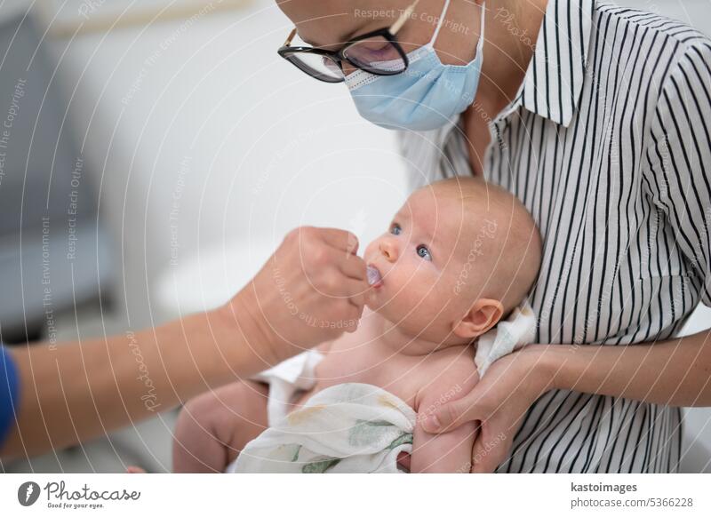 Pediatrician administring oral vaccination against rotavirus infection to little baby in presence of his mother. Children health care and disease prevention