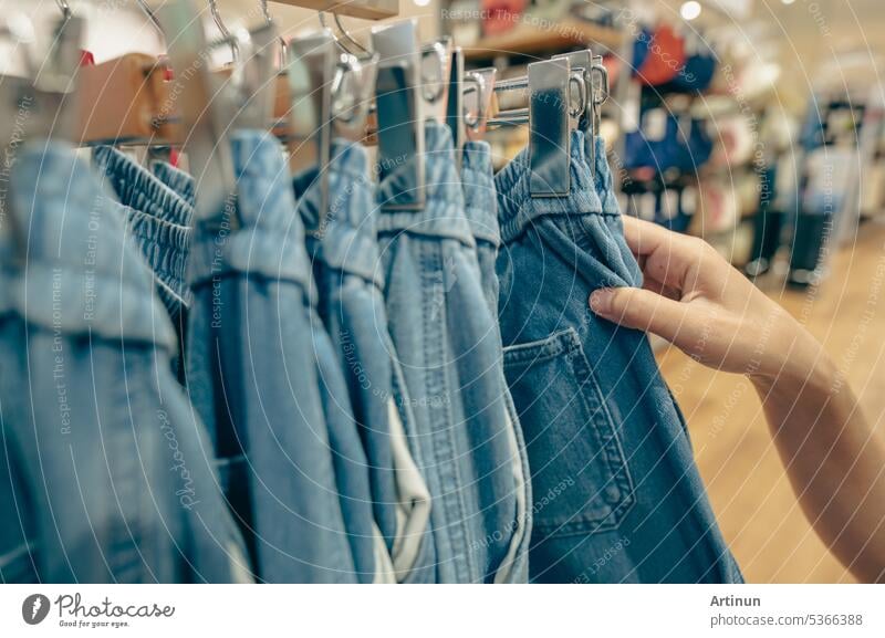 Woman shopping denim pants in clothing store. Woman choosing clothes. Jeans on hanger hanging on rack in clothing store. Fashion retail shop inside shopping mall. Clothes on hangers in a clothes shop.