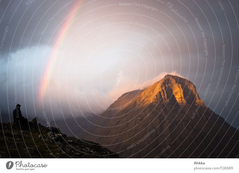 A man sits at the beginning of a rainbow on a peak, behind him a peak shines in the sun all lined with dramatic clouds Adventure Far-off places Life 1