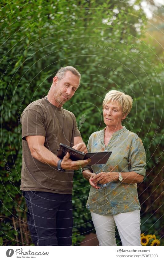 Craftsman being a gardener talking to a female senior customer holding a digital tablet making an offer craftsman woman explaining showing outside concept