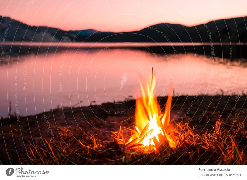 Bonfire. Small campfire with gentle flames beside a lake during a glowing sunset. San Juan night on the beach. People jumping over the bonfires. Bonfire at night.