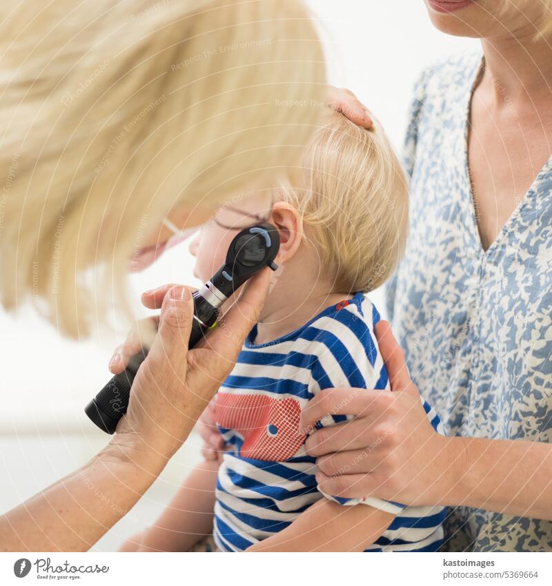 Infant baby boy child being examined by his pediatrician doctor during a standard medical checkup in presence and comfort of his mother. National public health and childs care care koncept.