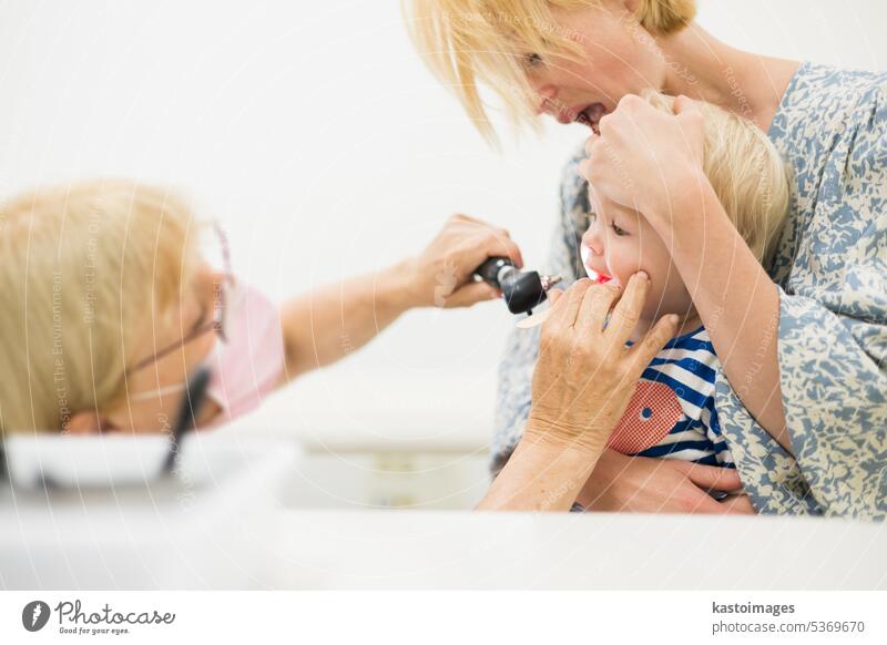 Infant baby boy child being examined by his pediatrician doctor during a standard medical checkup in presence and comfort of his mother. National public health and childs care care koncept.