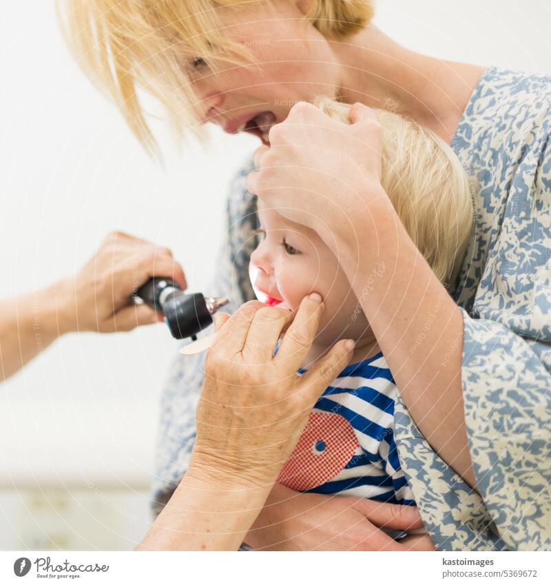 Infant baby boy child being examined by his pediatrician doctor during a standard medical checkup in presence and comfort of his mother. National public health and childs care care koncept.