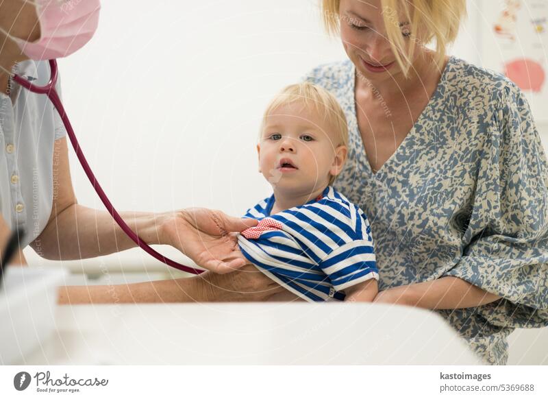 Infant baby boy child being examined by his pediatrician doctor during a standard medical checkup in presence and comfort of his mother. National public health and childs care care koncept.