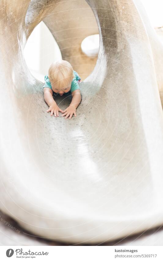 Child playing on outdoor playground. Toddler plays on school or kindergarten yard. Active kid on stone sculpured slide. Healthy summer activity for children. Little boy climbing outdoors.