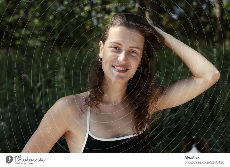 Portrait of young beautiful brunette smiling woman sitting in the sand in front of a forest warm Summery Beautiful weather plants proximity Day tranquillity