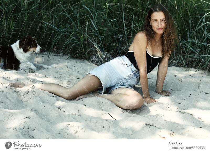 side portrait of young beautiful brunette smiling woman sitting in the sand in front of a forest warm Summery Beautiful weather plants proximity Day