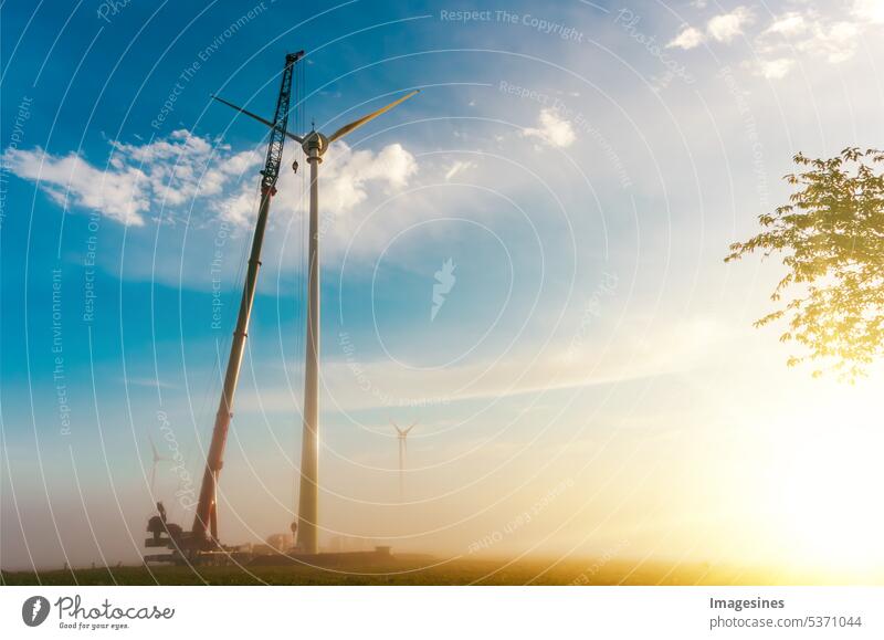 Wind turbine under construction at sunrise in fog. Crawler crane - machinery. Construction and assembly of a construction wind turbine by crane. Construction work on wind farm, Wörrstadt, Germany.