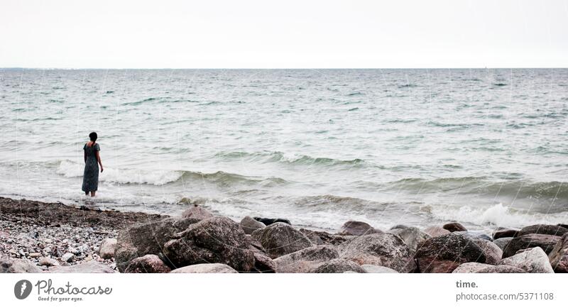 The young woman and the sea Woman Ocean Baltic Sea Waves stones Beach Sand Stand look Water coast Sky Horizon Nature Landscape Vacation & Travel Relaxation