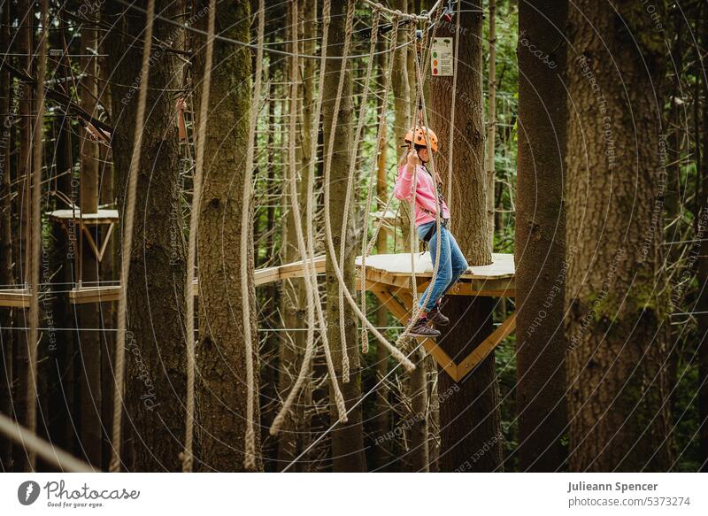 Child on rope high climber outdoors amongst trees treetop tree top climb harness girl ropes highwire extreme activity adventure nature active challenge height