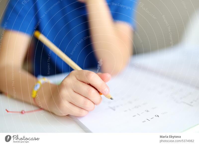 Elementary student boy doing homework at home. Child learning to count, solves arithmetic examples, doing exercises in workbook. Math tutorial. Preparing preschooler baby for school. Education