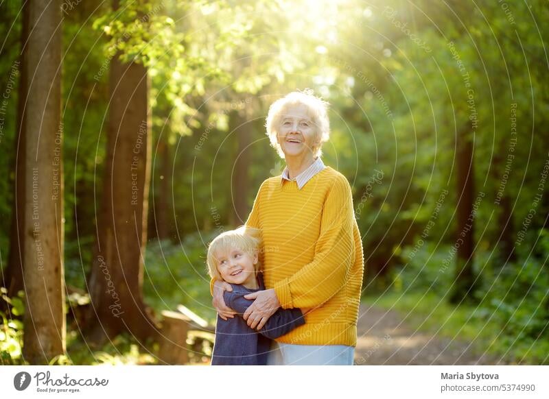 Loving grandson tenderly embracing his joyful elderly grandmother during walking at summer park. Two generations of family. senior old child hug embrace mom