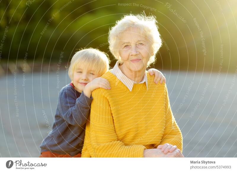 Loving grandson tenderly embracing his joyful elderly grandmother during walking at sunny summer park. Two generations of family. senior old child hug embrace