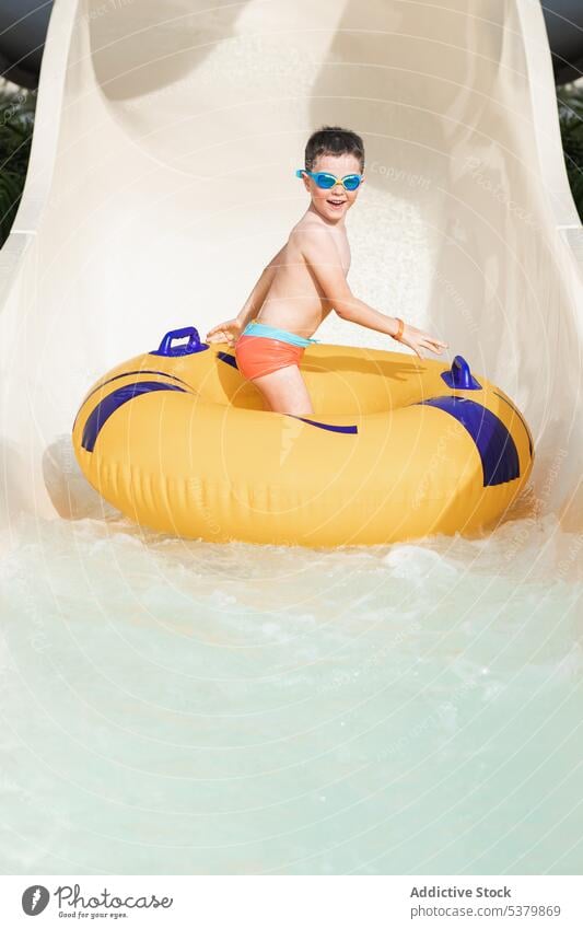 Happy child standing sideways on a ring on the water slide boy having fun kid enjoy park wet hair inflatable smile summer weekend childhood carefree happy