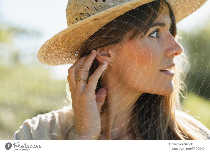 Young woman in straw hat standing in countryside smile touch head portrait happy vacation optimist glad summer young female cheerful sunlight gesture positive