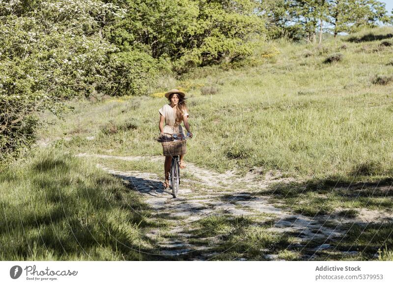 Woman riding bicycle in countryside woman ride nature summertime carefree fun happy female straw hat overall style rural long hair natural grassy fresh flower