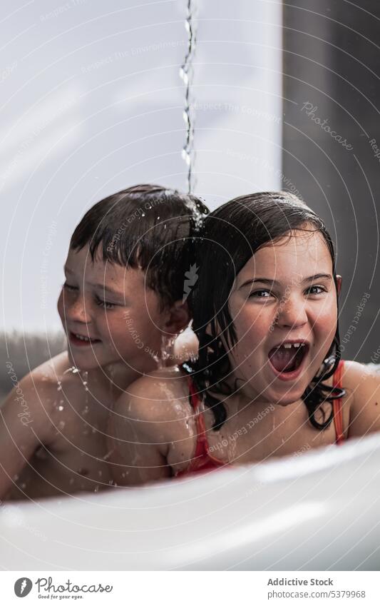 Happy children having fun in pool under falling water kid sibling happy cheerful bathtub smile mouth opened enjoy swimwear excited boy positive girl playful