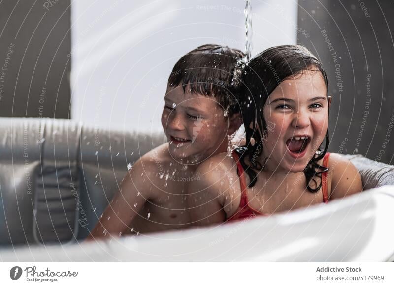 Happy children having fun in pool under falling water kid sibling happy cheerful bathtub smile girl boy mouth opened enjoy swimwear excited positive playful