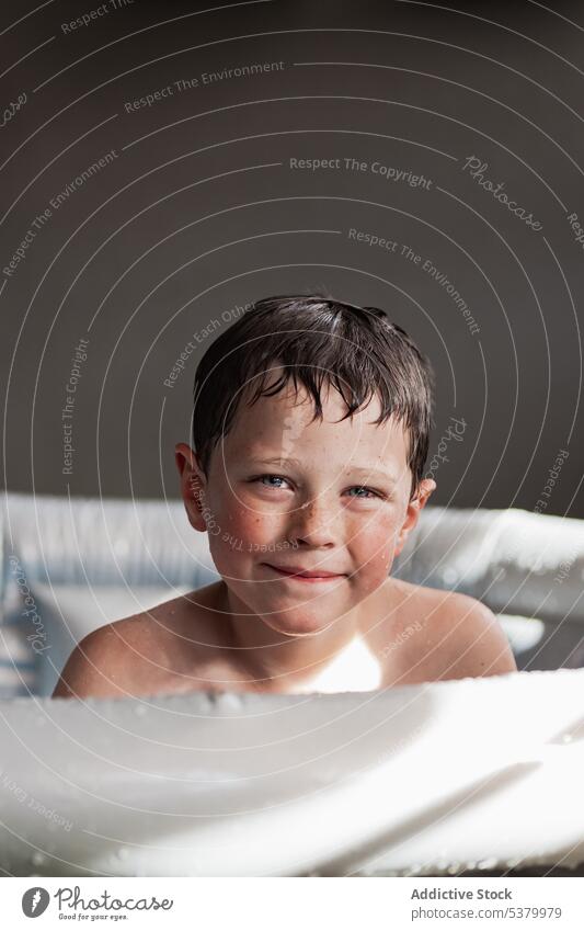 Cute kid with wet hair sitting in inflatable pool child portrait smile happy summer adorable shirtless relax boy childhood cheerful sunlight preteen cute