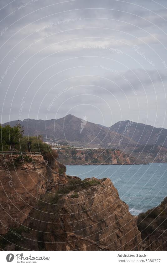 Amazing view of mountains around sea under cloudy sky rocky cliff landscape picturesque nature formation calm coast scenery tranquil hill ripple water