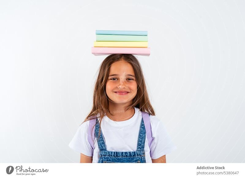 Smiling schoolgirl with books on head kid colorful stack balance smile pile uniform child positive education pupil happy little apron knowledge literature glad