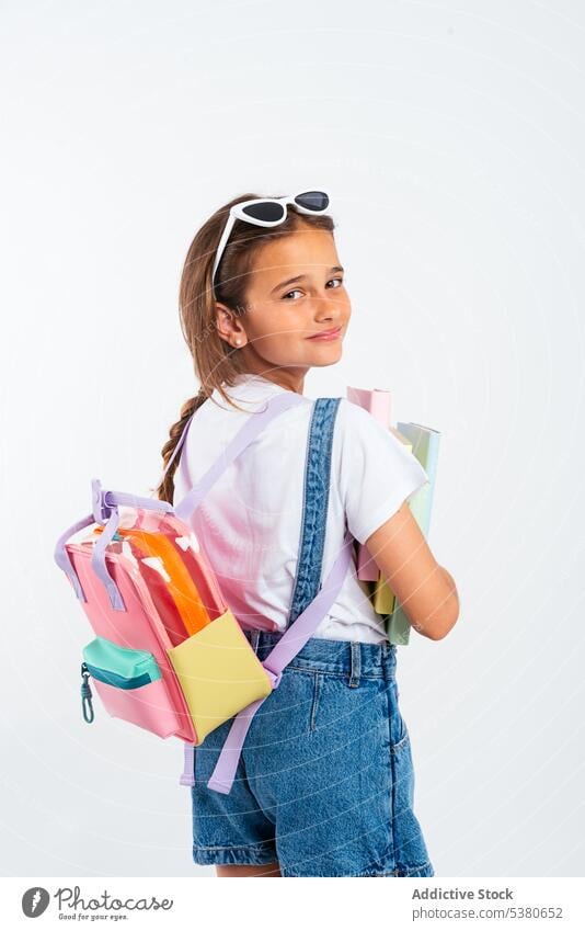 Schoolgirl with backpack and textbooks colorful child kid sunglasses little overall pupil denim childhood schoolgirl studio shot happy positive innocent eyewear