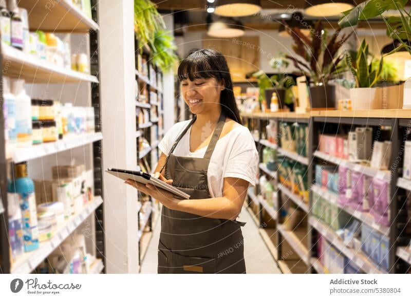 Cheerful Asian woman with tablet in store shop seller florist goods smile work owner small business female shelf asian young ethnic happy retail staff job