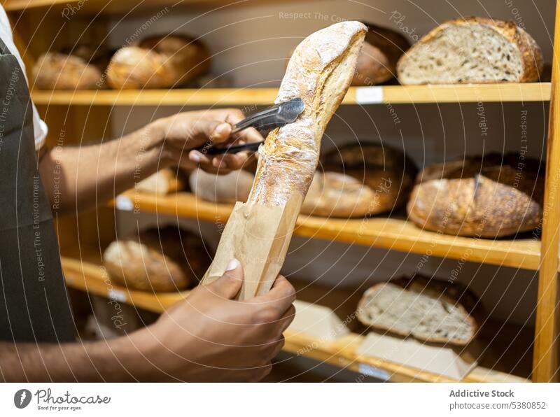 Unrecognizable black man putting bread in paper bag anonymous bakery seller grocery shop small business work baked owner food staff male pastry job store