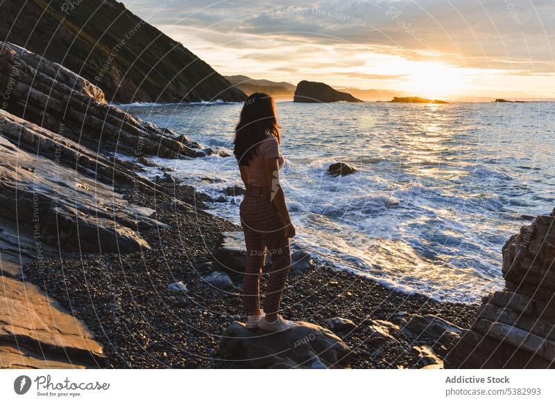 Anonymous woman admiring sea during sunset ocean coast shore beach nature admire sundown traveler wave rocky spain cloudy water seashore sky seaside summer