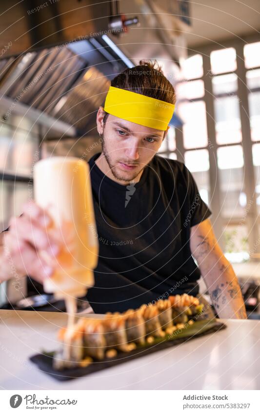 Focused young man adding sauce on gunkan maki cook concentrate delicious garnish tasty counter sushi prepare kitchen japanese male chef asian food restaurant