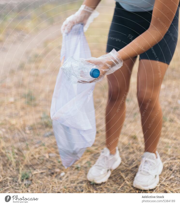 Anonymous crop woman picking up trash from the ground activist bag bottle care clean collect collecting day dirty earth ecology environment forest garbage glove