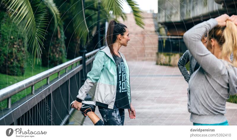 Woman runner stretching leg next to her female friends before training woman group team women together friendship running sport brunette ponytail exercise three