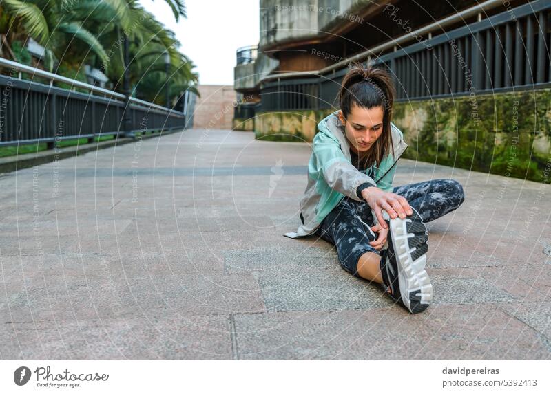 Happy woman runner stretching leg before training on town female arm exercise sitting floor warming up happy smile outside urban copy space girl brunette