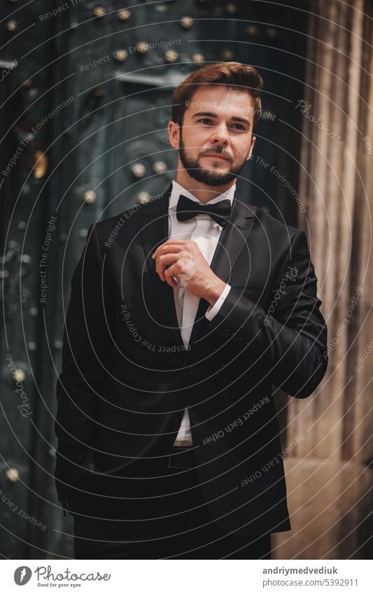 portrait of a stylish young groom in an old European town. man in a stylish suit with bow tie near old building. wedding day white pants montenegro kotor shirt