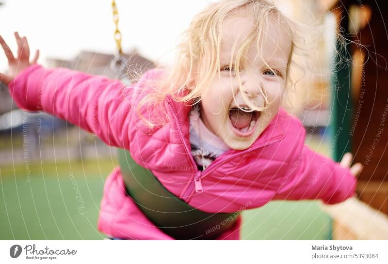 Cute little girl having fun on outdoor playground. Spring or summer active sport leisure for kids. Child on plastic swing laughing emotion backyard happy